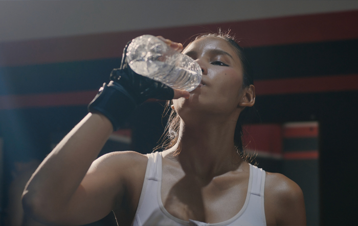 kobieta-pije-wode-po-treningu-w-silowni-bolero-sport Kobieta po treningu pije wodę z butelki w siłowni, uzupełniając elektrolity i dbając o nawodnienie