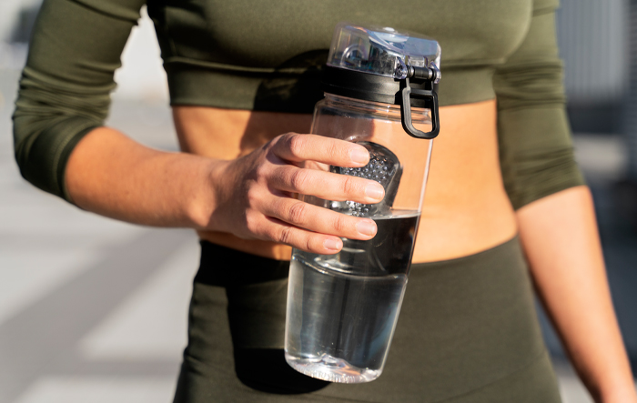 kobieta-trzyma-butelke-z-woda-po-treningu Kobieta w stroju sportowym trzyma butelkę z wodą po treningu na świeżym powietrzu