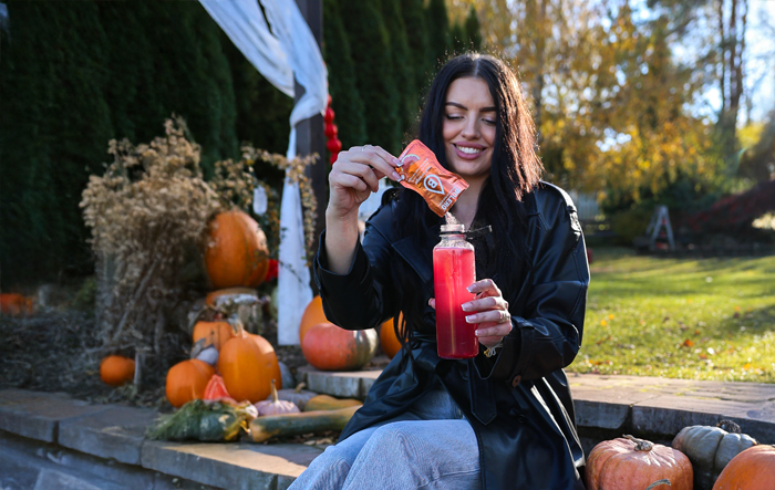 Kobieta wsypuje saszetkę Bolero do butelki z wodą, przygotowując nap&oacute;j w podr&oacute;ży
