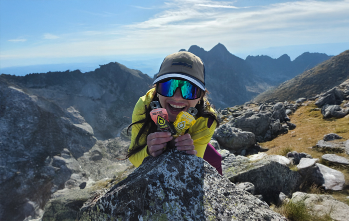 Turystka w g&oacute;rach trzyma saszetki Bolero podczas aktywnej podr&oacute;ży
