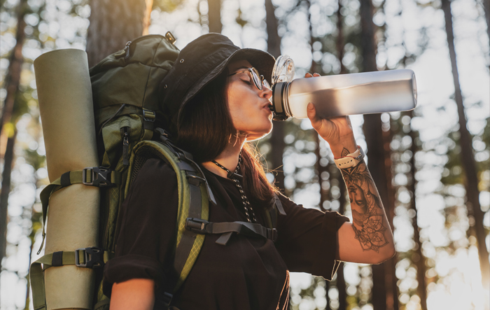 Turystka z plecakiem pije wodę z butelki podczas wędr&oacute;wki w lesie