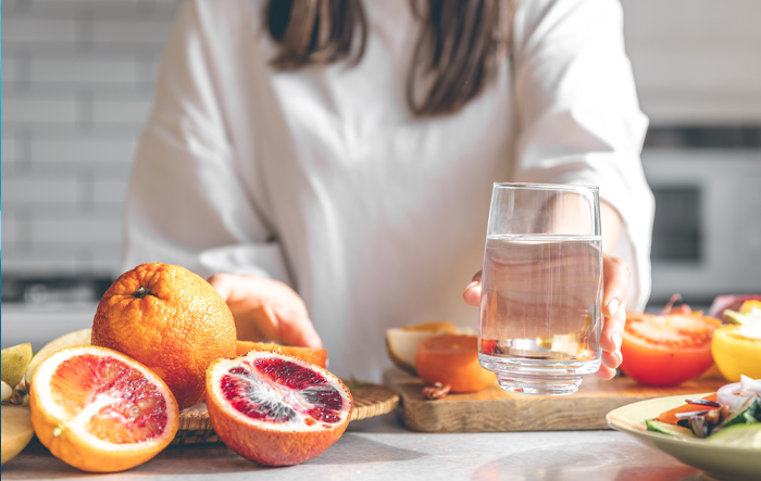 Szklanka wody i owoce na stole – codzienne nawodnienie i rola elektrolitów dla zdrowia