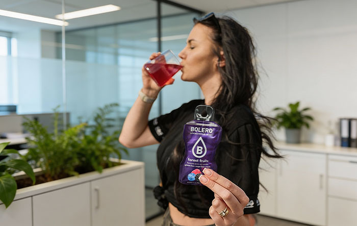 Kobieta pije napój Bolero w biurze, trzymając saszetkę z napojem bez cukru