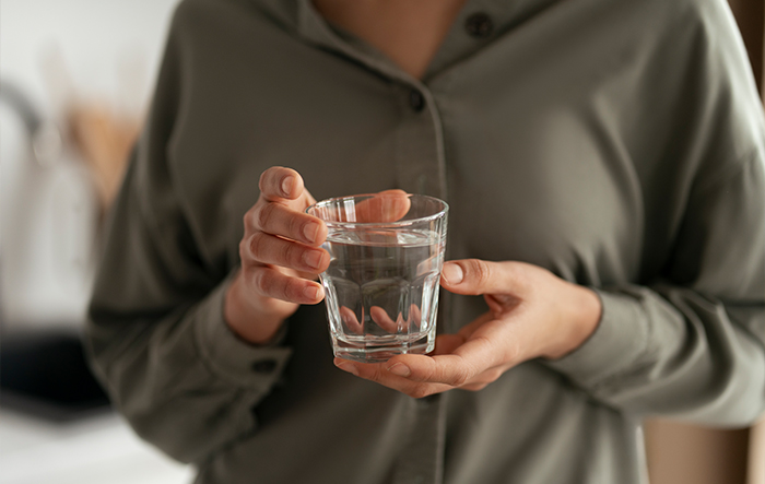 Szklanka wody trzymana w dłoniach jako symbol świadomego i spokojnego nawadniania