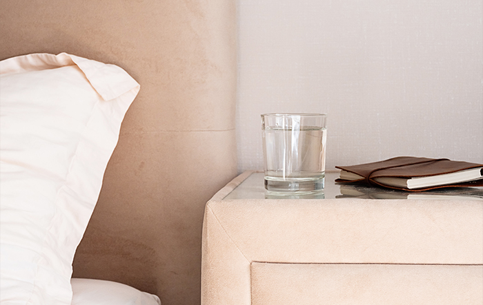 Szklanka wody na stoliku nocnym obok łóżka - nawodnienie przed snem