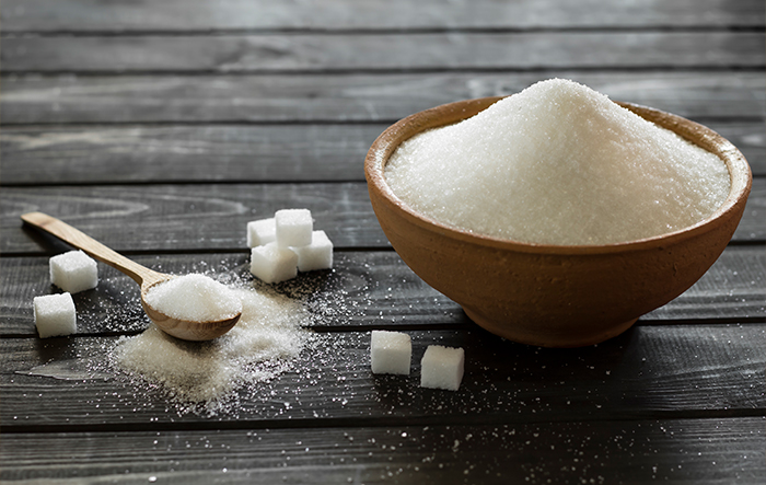 Miska z białym cukrem i kostki cukru na drewnianym stole &ndash; symbol wysokiego spożycia cukru.