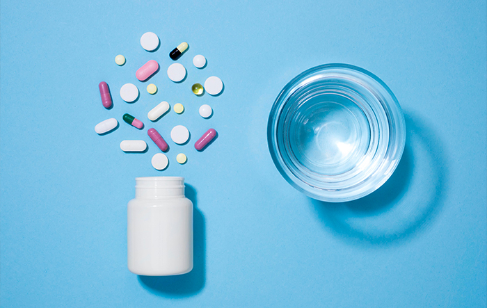 Tabletki i kapsułki obok szklanki wody &ndash; niekt&oacute;re leki i suplementy mogą nasilać uczucie pragnienia.