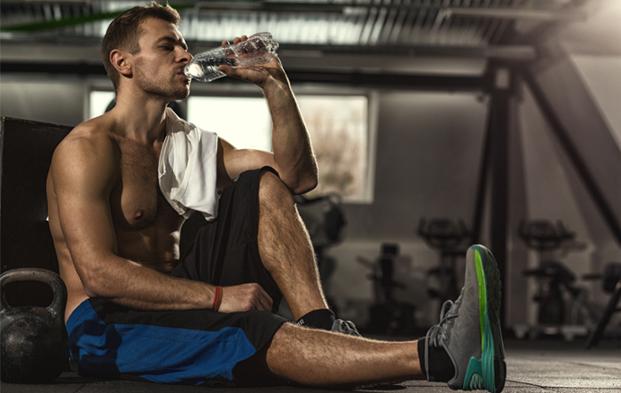 Mężczyzna odpoczywający po treningu na siłowni i pijący wodę – wsparcie regeneracji z Bolero Energy dla sportowców