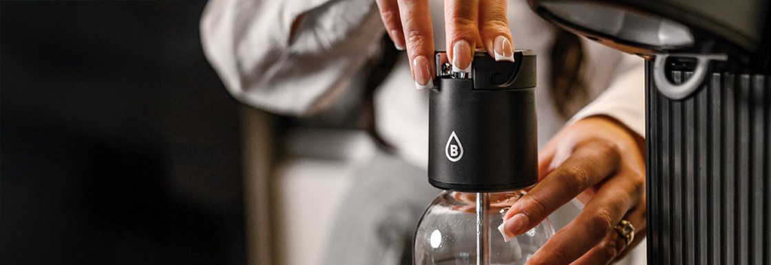 Zbliżenie na zakładanie głowicy Bolero Soda Maker na butelkę z napojem