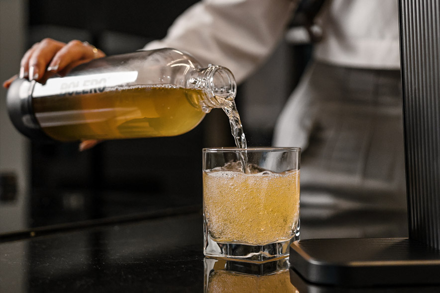 Gotowy gazowany napój jest przelewany z butelki do szklanki z widocznymi bąbelkami. Bolero soda maker