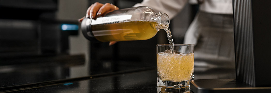 Gotowy gazowany napój jest przelewany z butelki do szklanki z widocznymi bąbelkami. Bolero soda maker