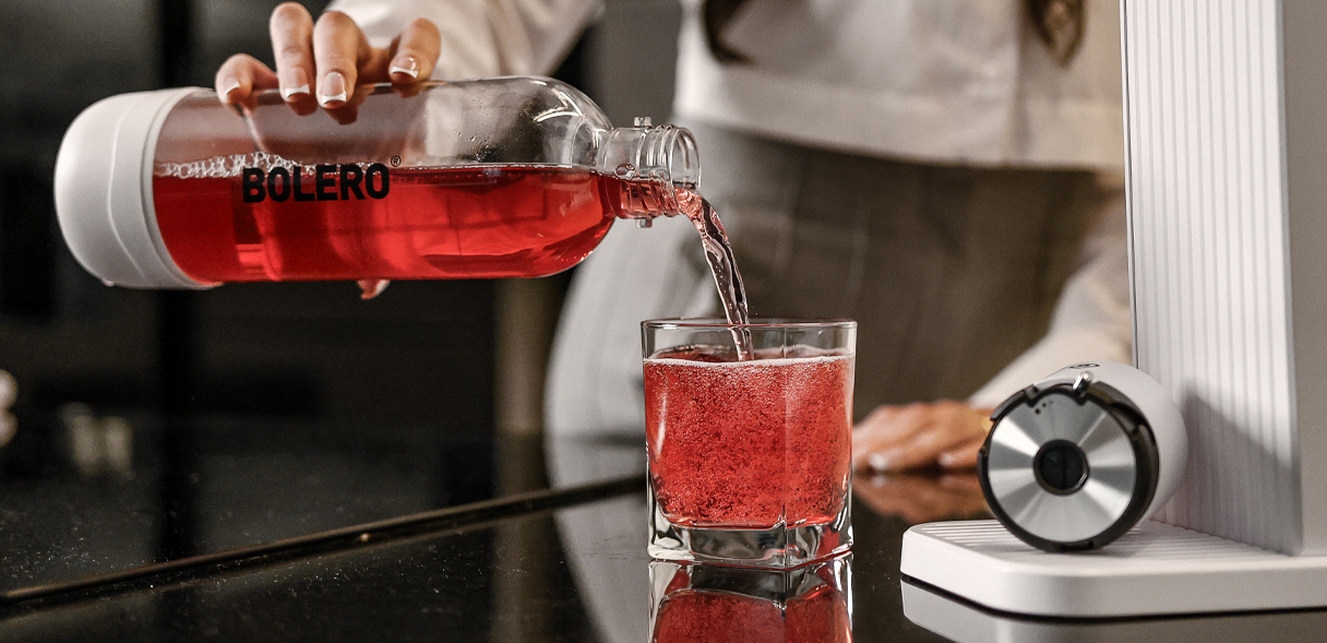 Butelka Bolero z czerwonym napojem nalewanym do szklanki na blacie kuchennym.