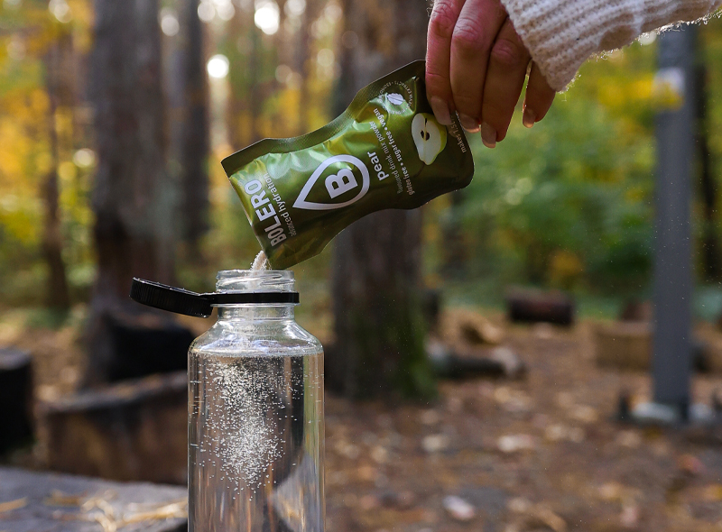 Przygotowanie napoju Bolero Pear – wsypywanie saszetki o smaku gruszki do butelki z wodą, napój bez cukru i glutenu, idealny na świeżym powietrzu.