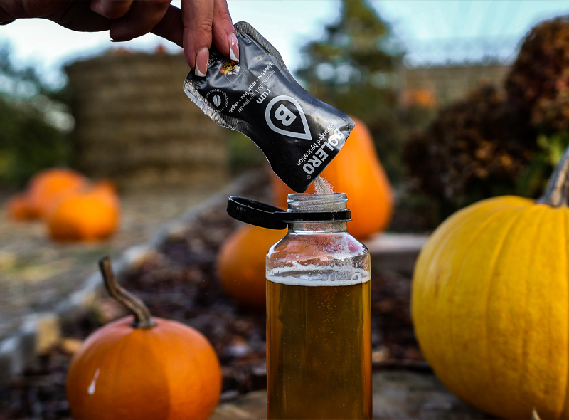 Przygotowanie napoju Bolero Rum – wsypywanie saszetki do butelki z wodą, jesienny klimat z dyniami w tle, napój bez cukru o smaku rumu.