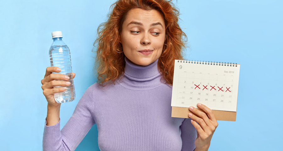 Kobieta trzyma wodę i kalendarz z zaznaczonymi dniami miesiączki kontekst picie wody a PMS