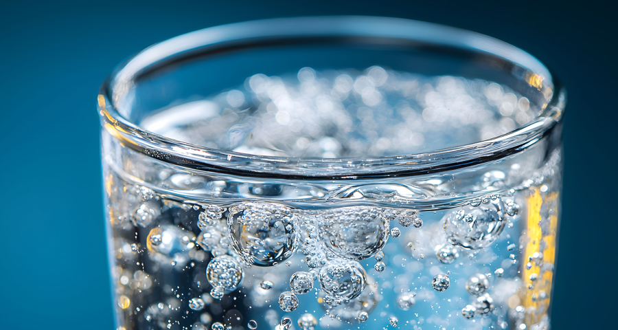 Szklanka świeżo gazowanej wody z widocznymi bąbelkami dwutlenku węgla na tle w chłodnym, niebieskim odcieniu.