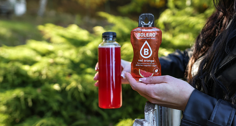 Kolorowy napój Bolero bez cukru przygotowany z saszetki, trzymany w dłoni na tle zieleni