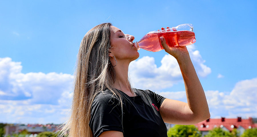 Kobieta pije kolorowy napój Bolero bez cukru podczas codziennego nawodnienia na świeżym powietrzu