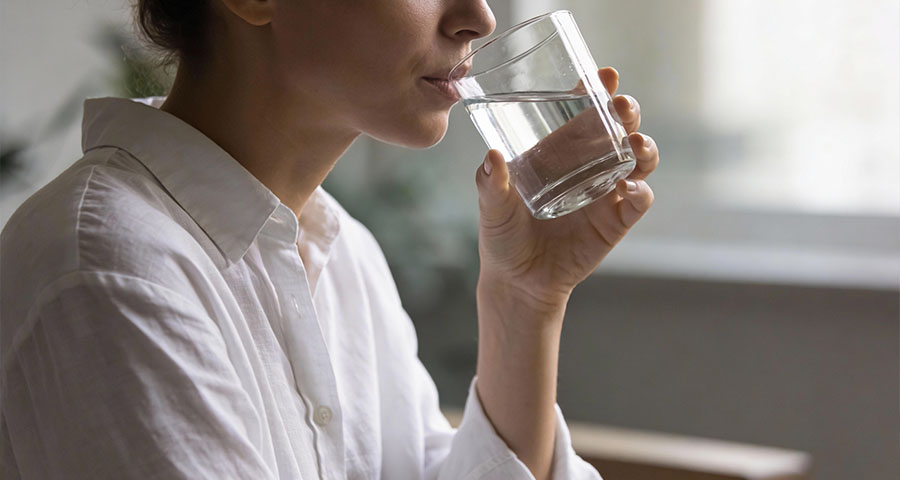 Kobieta pije wodę ze szklanki, zastanawiając się, czy lepiej pić małymi łykami czy większymi porcjami