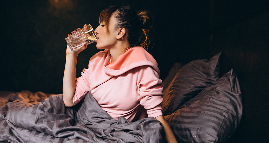 Kobieta pijąca szklankę wody wieczorem w łóżku – picie wody przed snem