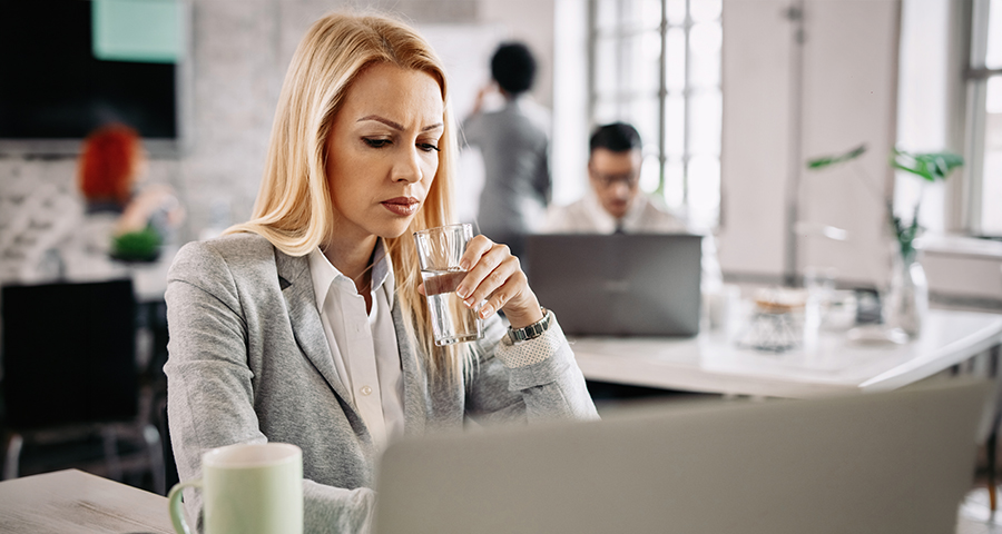 Kobieta w biurze pije wodę i zastanawia się, dlaczego ciągle chce jej się pić