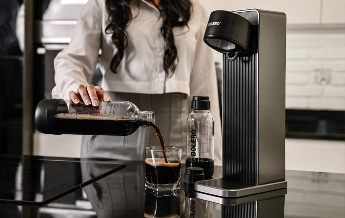 Zbliżenie szklanki wody w rękach kobiety w kuchni, obok świeżych owoc&oacute;w