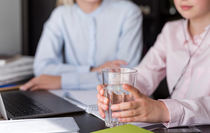 Zbliżenie szklanki wody w rękach kobiety w kuchni, obok świeżych owoc&oacute;w